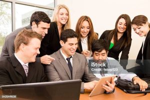 Mixed-age, multi-ethnic group of business people using digital tablet and laptop computer at a desk during an office meeting.  Office setting, window background.  Technology.